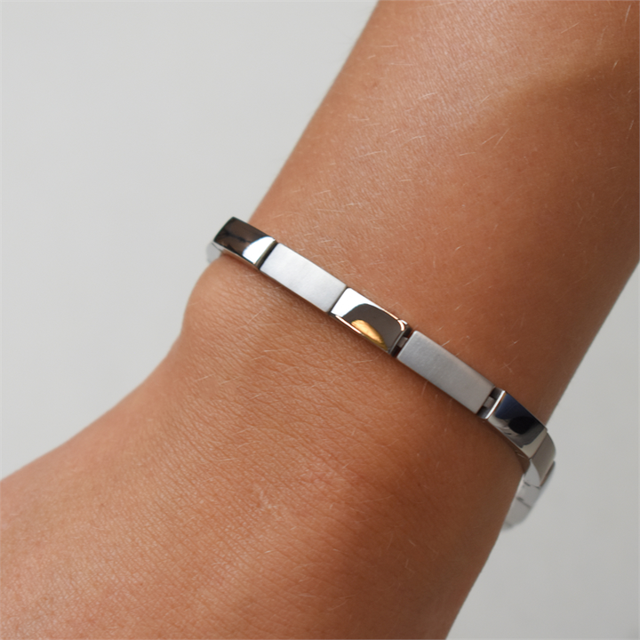 Een close-up van een pols met de Boccia Titanium Armband 03036-01 van Boccia. Deze armband heeft een minimalistisch, gepolijst ontwerp, is gemaakt van duurzaam materiaal en heeft een effen achtergrond.