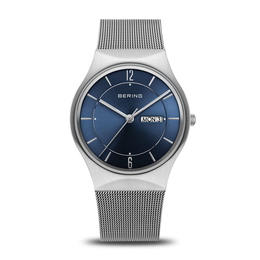 De 11938-003DD van Bering is een strak horloge met een zilveren meshband en een ronde blauwe wijzerplaat. Het heeft quartzprecisie met zilveren uurmarkeringen, wijzers, dag-/datumweergave aan de rechterkant en Bering bovenaan, allemaal beschermd door duurzaam saffierglas.