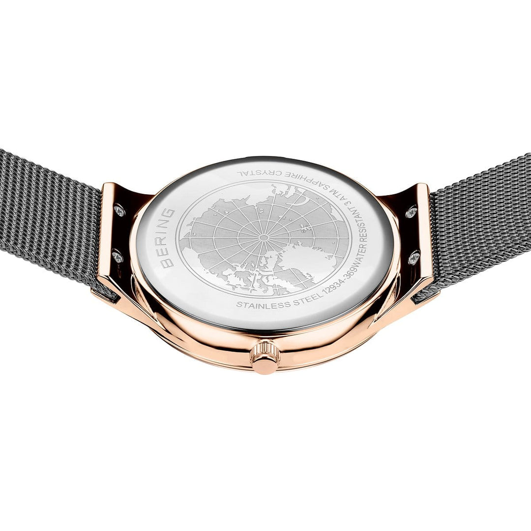 De Bering 12934-369 heeft een roestvrijstalen meshband met roségouden afwerking en een quartz-uurwerk. De achterkant toont een ingewikkeld gegraveerde wereldkaart, met etsen die details over de constructie van roestvrij staal en saffierglas benadrukken.