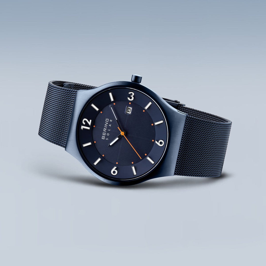 Het Bering 14440-393 horloge is voorzien van Saffierglas voor krasbestendigheid, een strak marineblauw ontwerp met een mesh band en een ronde wijzerplaat met grote witte cijfers, oranje minutenmarkeringen en een datumweergave op 6 uur. Het Solar-uurwerk mechanisme zorgt ervoor dat het tijdloze elegantie belichaamt.