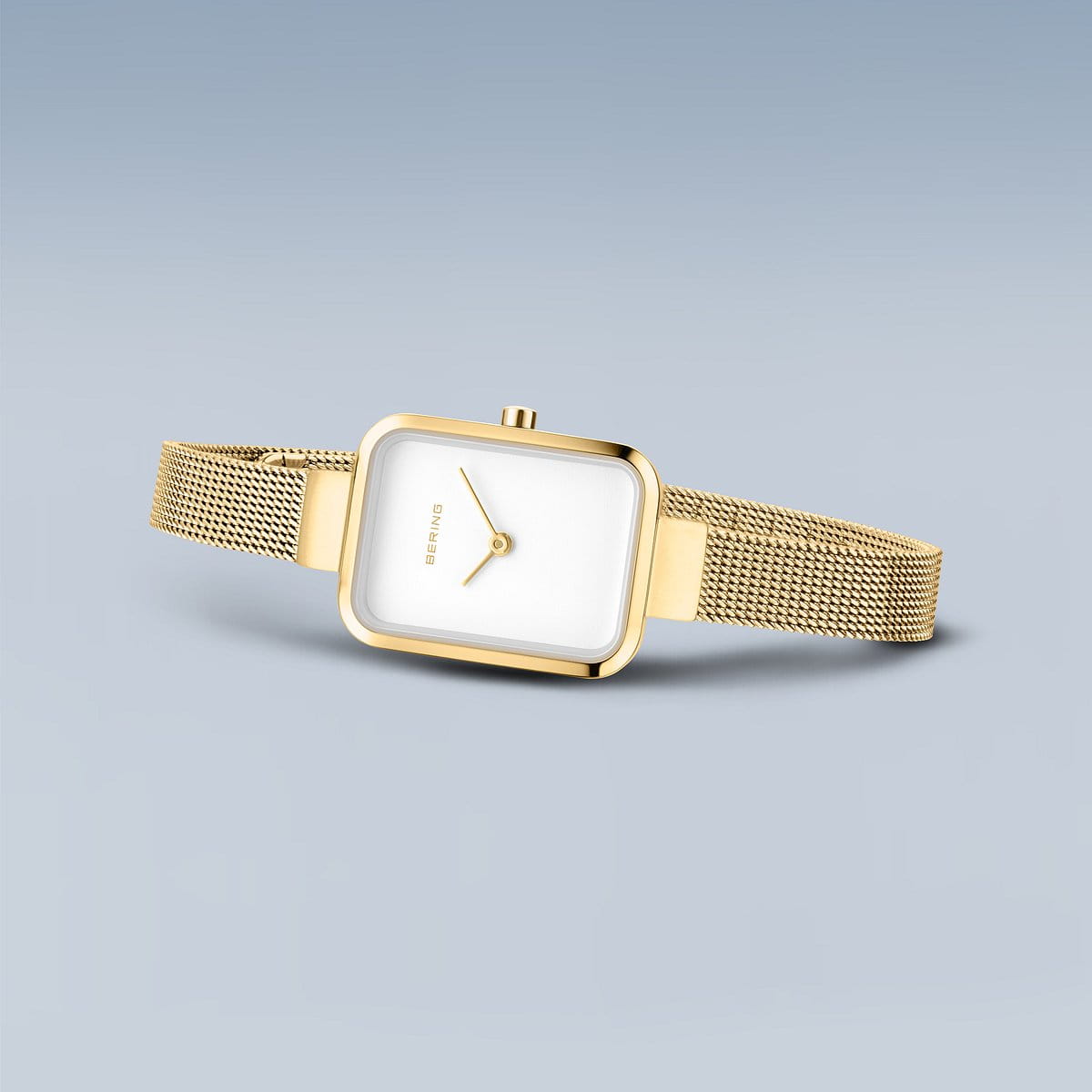 Het Bering horloge 14520-334 wordt getoond tegen een lichtblauwe achtergrond. Dit goudkleurige model heeft een vierkante witte wijzerplaat, minimalistisch design, mesh metalen band en gouden wijzers en roestvrijstalen kast.