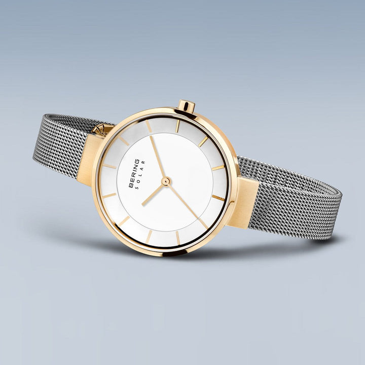Het Bering dameshorloge 14631-024 heeft een minimalistisch ontwerp met quartz-uurwerkprecisie, een kast met gouden accenten, een witte wijzerplaat, gouden uurmarkeringen en wijzers. Het heeft een elegante zilveren meshband en wordt weergegeven op een zachtblauwe gradiëntachtergrond.