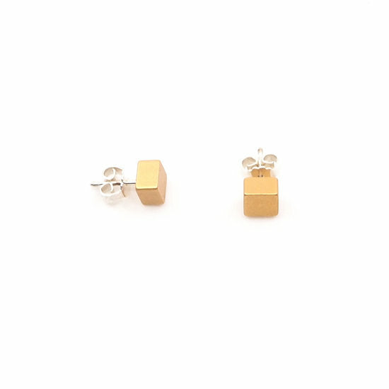 De Otra Cosa Gekleurde kubus oorbellen abricot zijn minimalistische gouden kubus oorbellen op een strak witte achtergrond, wat een vleugje verfijning toevoegt aan elke outfit.