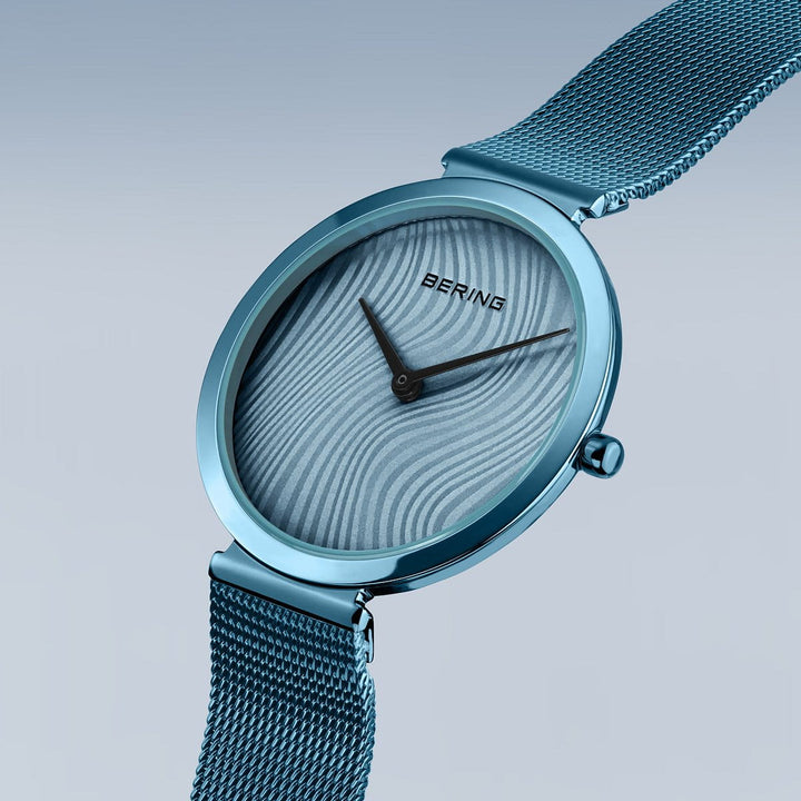 De Bering dameshorloge 18132-Charity2 heeft een minimalistische blauwe wijzerplaat, mesh band, zilverkleurige wijzers, quartz uurwerk, saffierglas en golvende patronen op het gezicht - perfect vormgegeven door Bering.