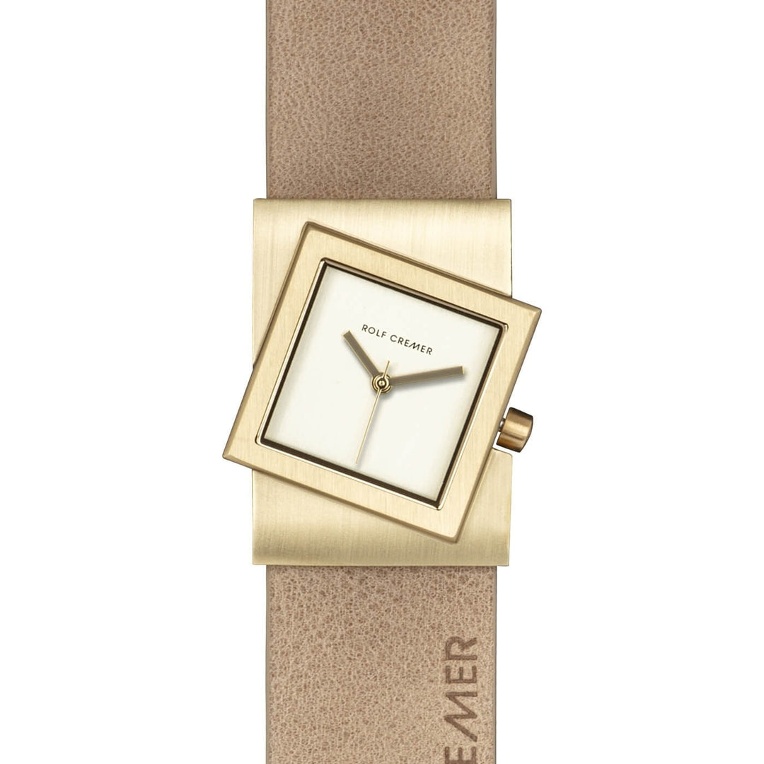 De Rolf Cremer Horloge 507703 Turn-S is een opvallend kwartshorloge met een vierkante wijzerplaat, een gekantelde goudkleurige kast en een beige band. De wijzerplaat belichaamt minimalistisch Deens design, bescheiden wijzers, vage markeringen en toont subtiel het merk Rolf Cremer op zowel de wijzerplaat als de band.