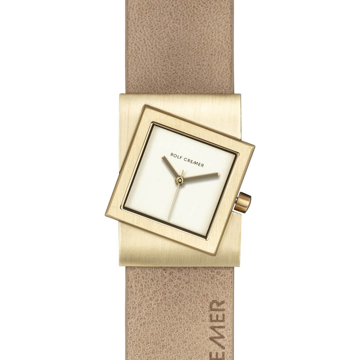 De Rolf Cremer Horloge 507703 Turn-S is een opvallend kwartshorloge met een vierkante wijzerplaat, een gekantelde goudkleurige kast en een beige band. De wijzerplaat belichaamt minimalistisch Deens design, bescheiden wijzers, vage markeringen en toont subtiel het merk Rolf Cremer op zowel de wijzerplaat als de band.