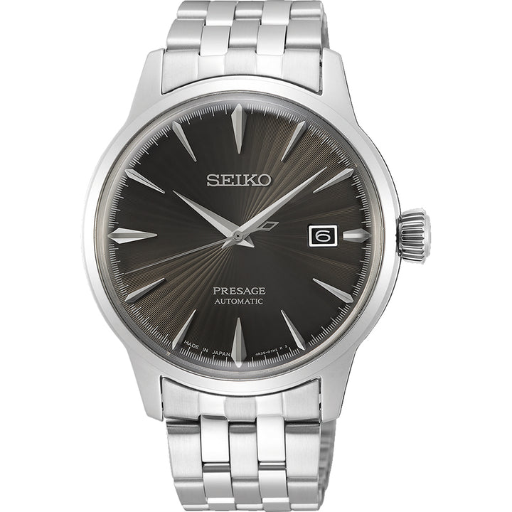 Het Seiko Presage heren horloge SRPE17J1 heeft een roestvrijstalen band, een donkere wijzerplaat met zonnestralenpatroon en zilveren uurmarkeringen, een datumvenster op 3 uur, een gecanneleerde kroon en het iconische Seiko-logo onder 12 uur.