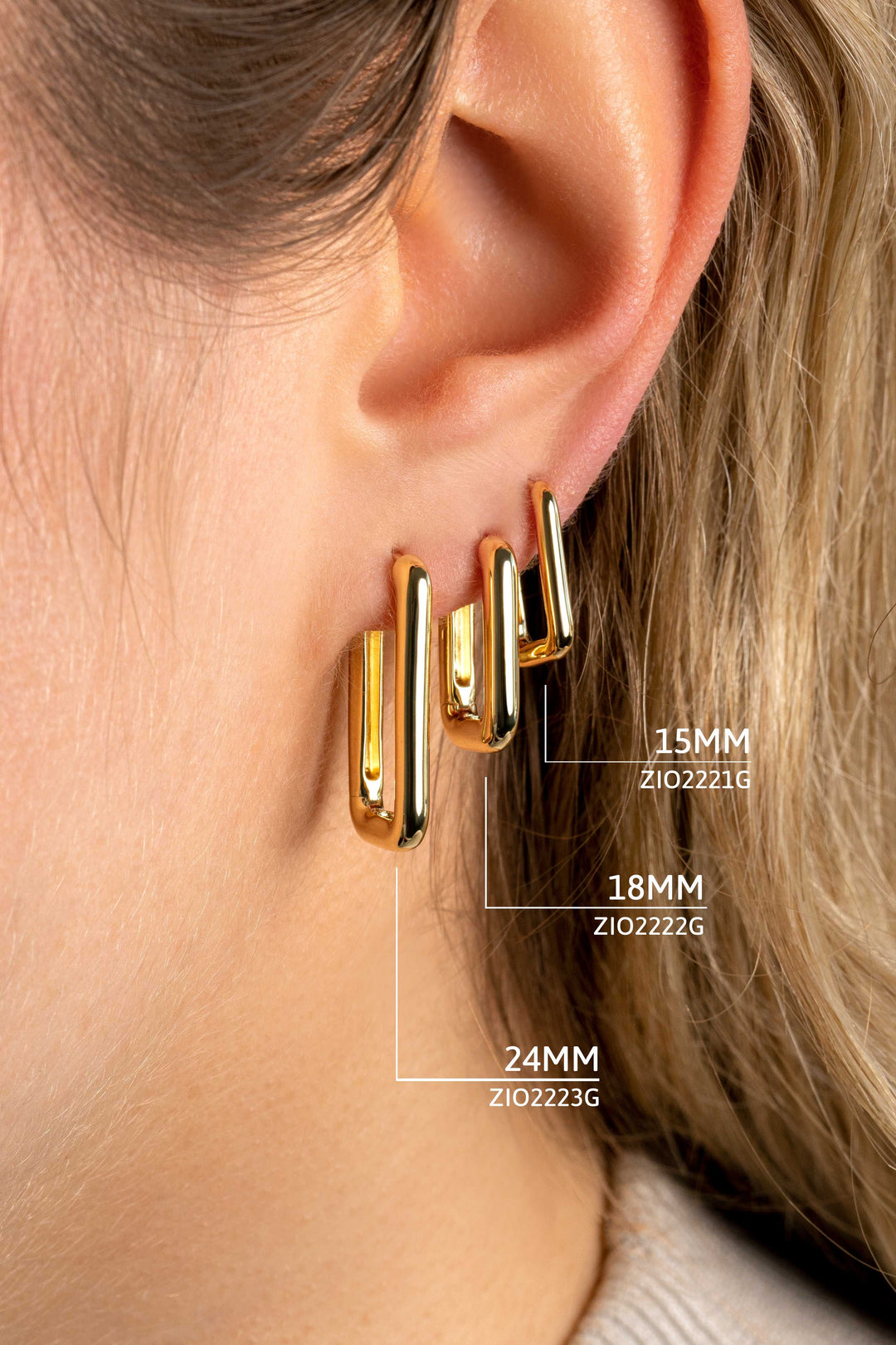 Een close-up van iemands oor met drie Zinzi Oorbellen Gold Plated Zio2221 G (14K goud verguld, 15mm, 18mm, 24mm), elk gelabeld op grootte en code - perfect te combineren met zilveren oorbellen.