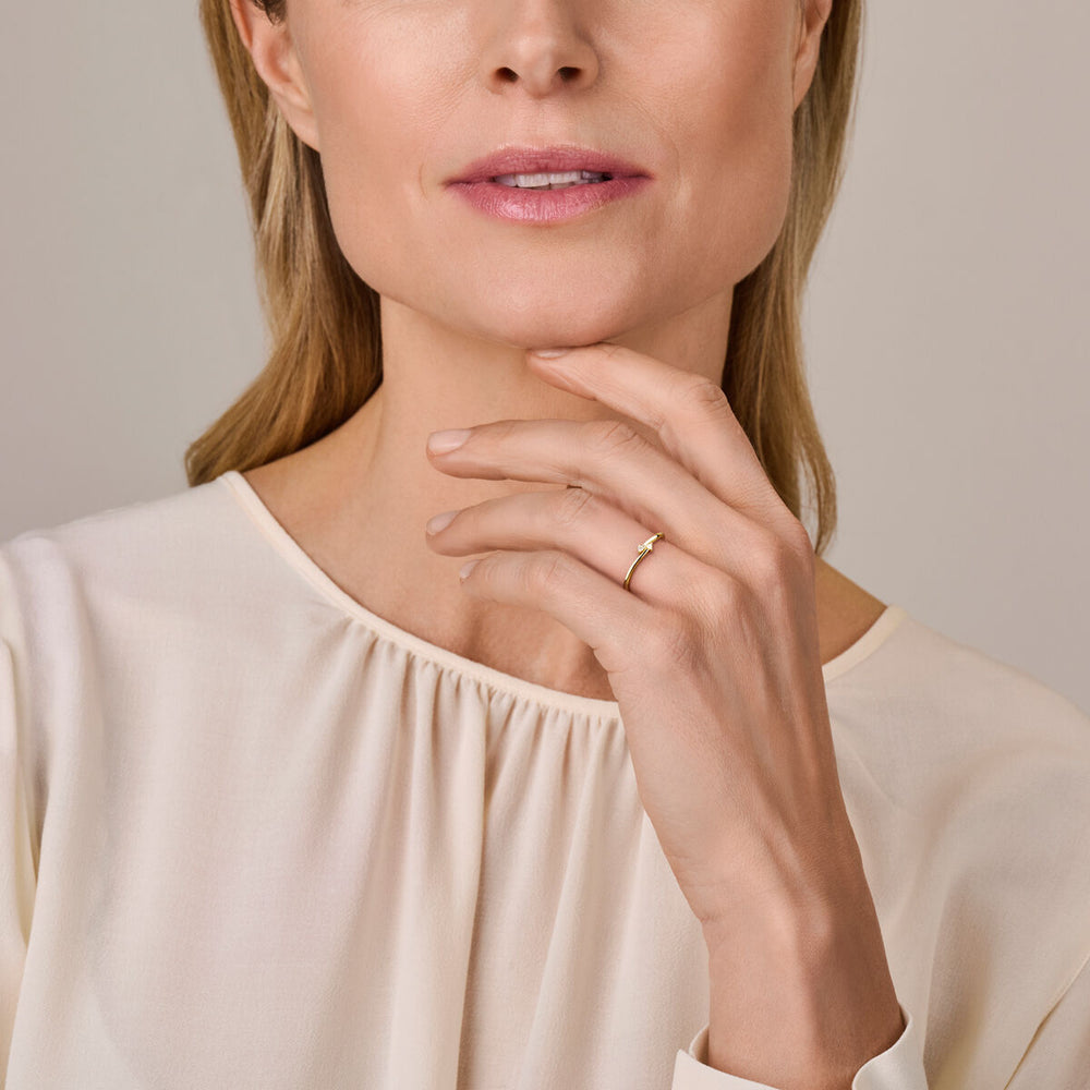 Een vrouw in een crèmekleurige blouse raakt zachtjes haar kin aan en toont een Van der Kooij Collectie ring diamant 0.03ct h si 14K geelgoud aan haar vinger; alleen de onderste helft van haar gezicht en bovenlichaam zijn zichtbaar.