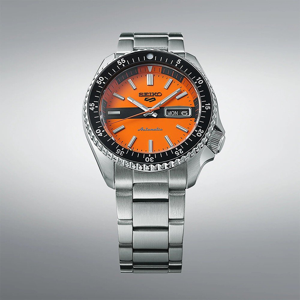 Het Seiko 5 Sports herenhorloge SRPK11K1 van Seiko heeft een strak zilveren design met een oranje wijzerplaat en automatisch uurwerk. Het heeft een zwarte lunette met minutenmarkeringen, zilveren uurmarkeringen en wijzers, waterdichtheid 10ATM, metalen schakelband en dag-datumweergave op 3 uur.