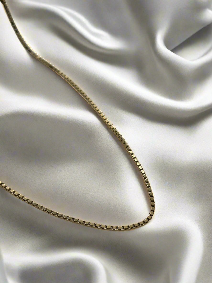 Een delicate vintage gouden collier 52cm venetiaans 18k 10gr van Juwelier van der Kooij rust op glad, wit satijn. Het licht benadrukt zachtjes de fijne details van de ketting - een prachtig stuk uit onze Vintage Collectie.