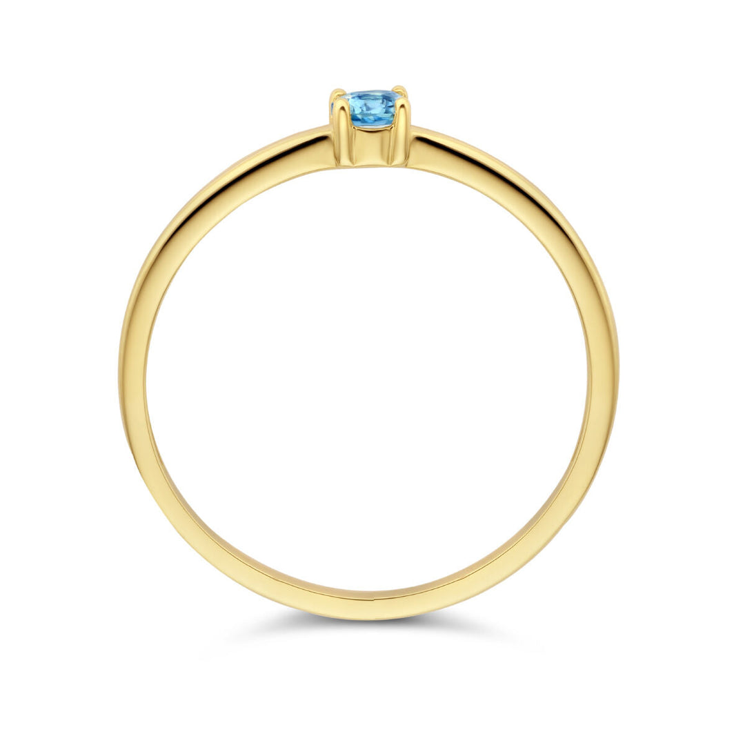 De Van der Kooij Collectie ring met geboortesteen blauwe topaas december is gemaakt van 14K geelgoud, met een dunne band en een kleine ronde blauwe topaas in een eenvoudige vierpoots zetting, getoond vanaf de zijkant tegen een witte achtergrond.