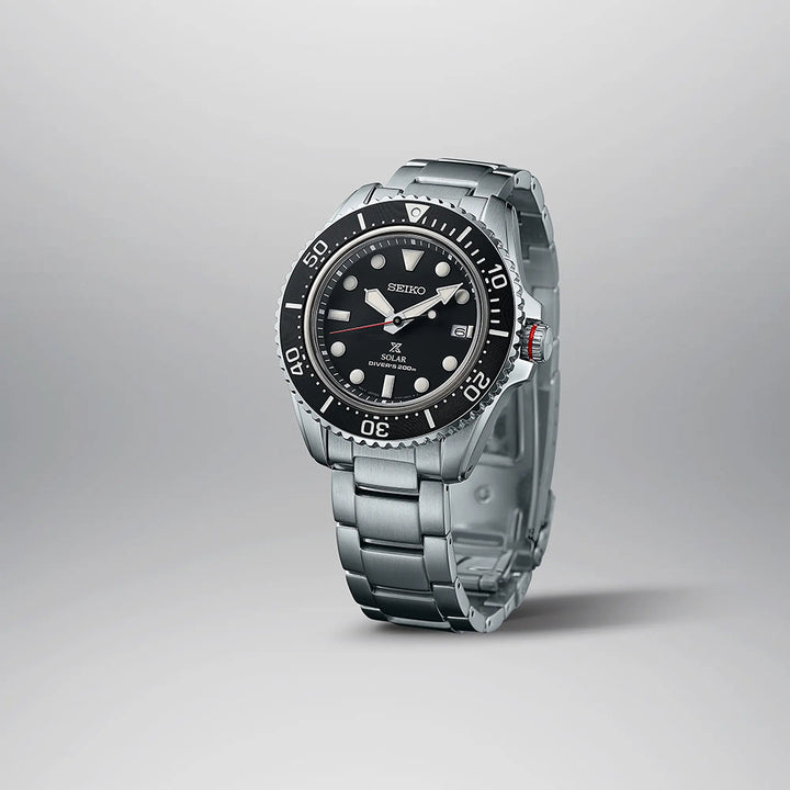 De Seiko Prospex heren horloge SNE589P1 is een strak zilveren duikhorloge met een zwarte wijzerplaat met grote witte uurmarkeringen en een datumvenster op drie uur. Het op zonne-energie werkende mechanisme en de minutenschaal op de lunette verbeteren de functionaliteit, terwijl de metalen armband elegantie uitstraalt.