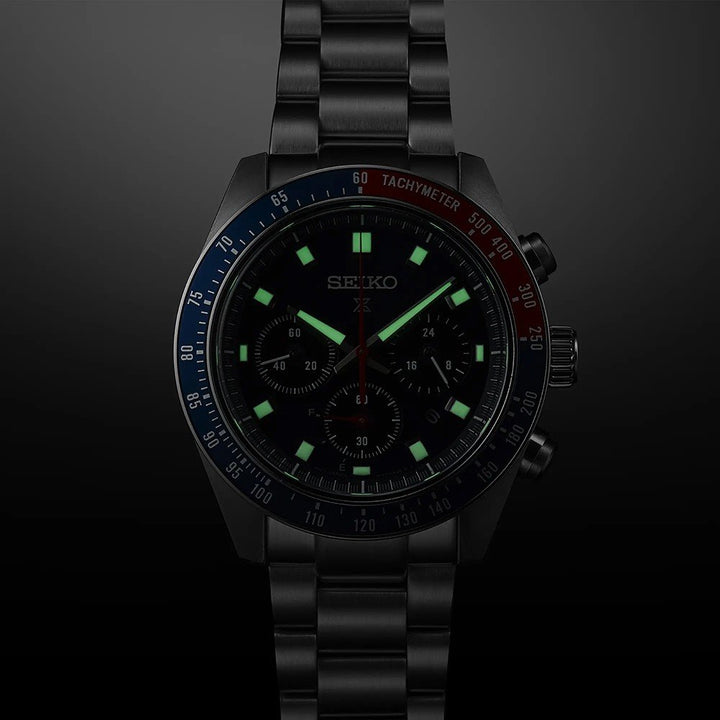Het Seiko Prospex herenhorloge SSC913P1 heeft lichtgevende groene markeringen en wijzers op een donkere achtergrond, een halfblauwe en rode lunette met tachymeterschaal, een solar uurwerk, een metalen schakelband en chronograaf-subwijzerplaten.