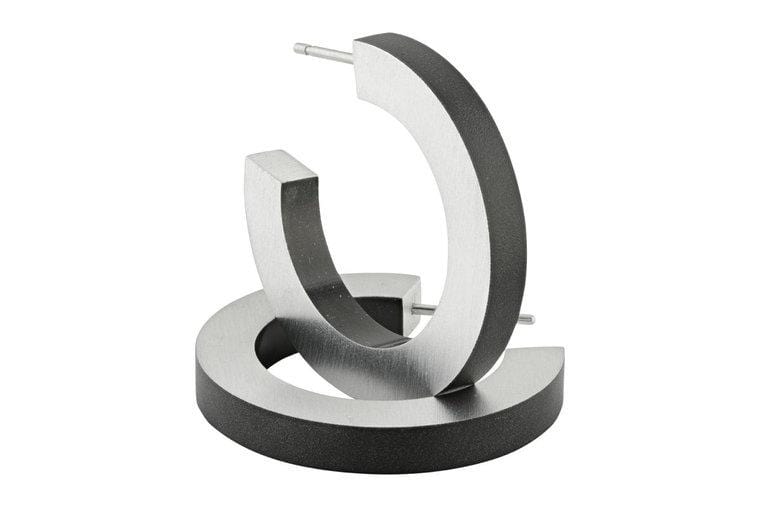 Twee moderne CLIC Creations Creolen Ronde ringen Zwart O10Z metallic open hoop oorbellen zijn gemaakt van hypoallergeen chirurgisch staal met een matte afwerking. Handgemaakt in Nederland, ze hebben een rechtopstaand en plat geometrisch ontwerp in een strakke grijze of zilveren tint.