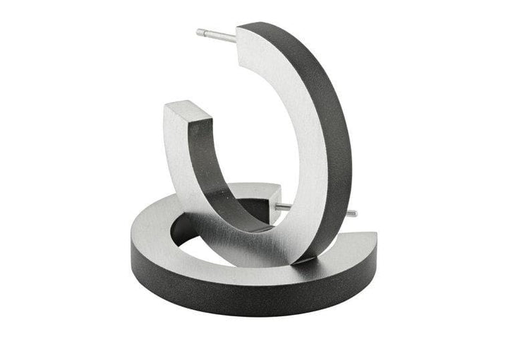 Twee moderne CLIC Creations Creolen Ronde ringen Zwart O10Z metallic open hoop oorbellen zijn gemaakt van hypoallergeen chirurgisch staal met een matte afwerking. Handgemaakt in Nederland, ze hebben een rechtopstaand en plat geometrisch ontwerp in een strakke grijze of zilveren tint.