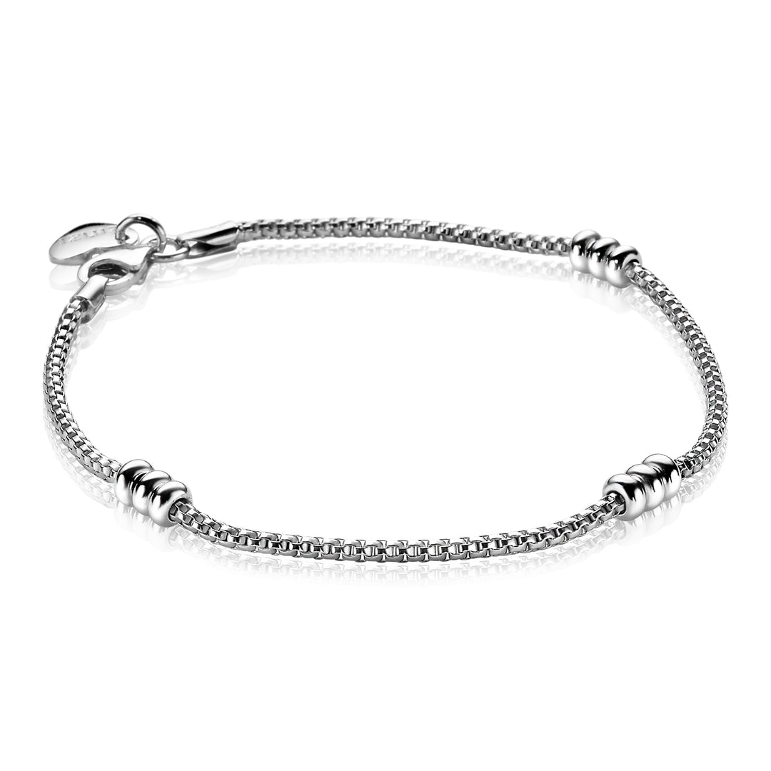 De Zinzi Armband Zilver Zia1421 is een delicate zilverkleurige armband met een dunne ketting en gelijkmatig verdeelde decoratieve kralen, met een hartvormige bedel bij de sluiting. Getoond tegen een witte achtergrond, belichaamt het de elegantie van het merk Zinzi.