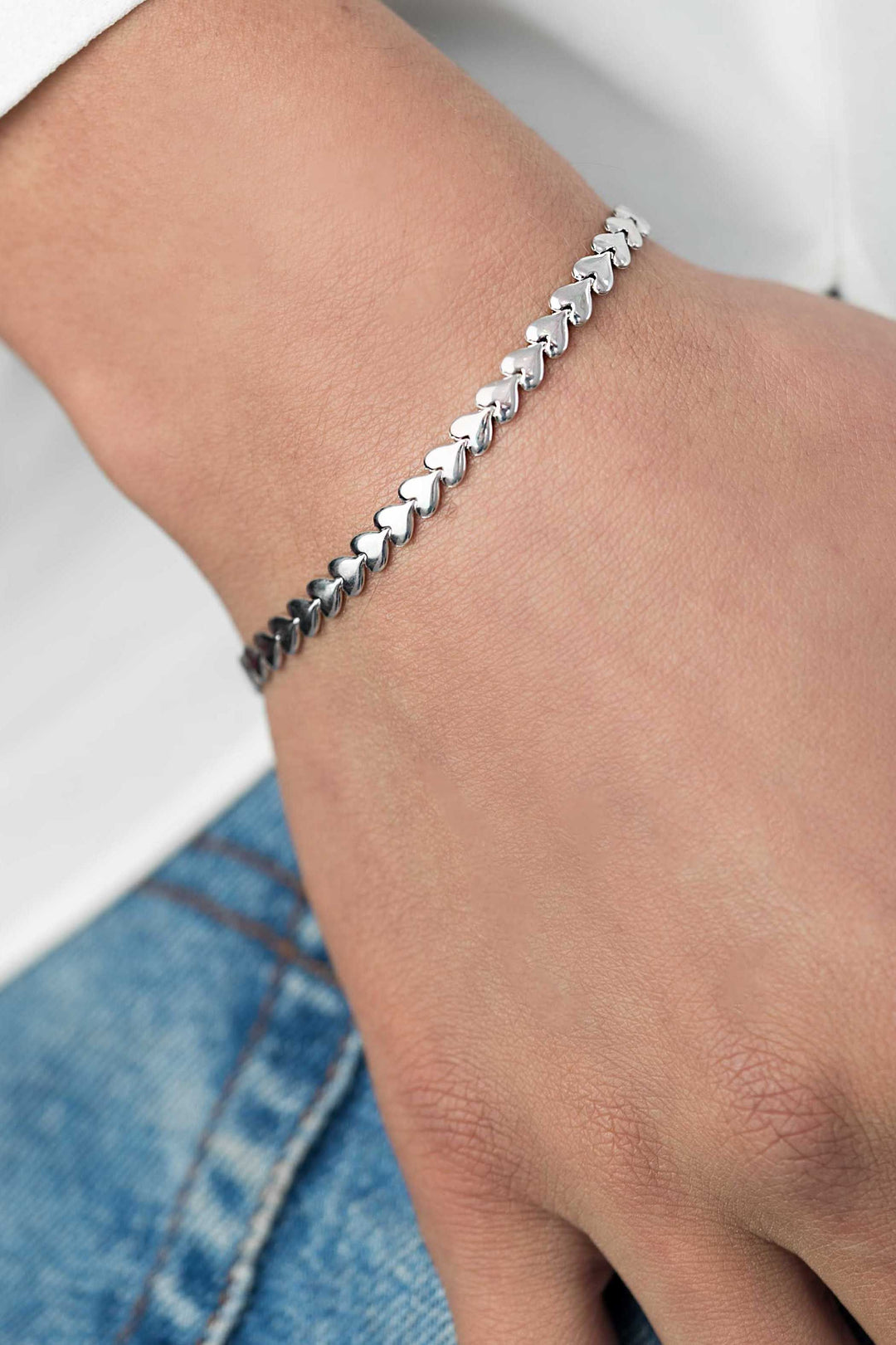 Een close-up van een pols versierd met de Zinzi Armband Zilver Zia1798 van Zinzi, met kleine hartjes, gestyled met een blauwe jeans en een wit overhemd.