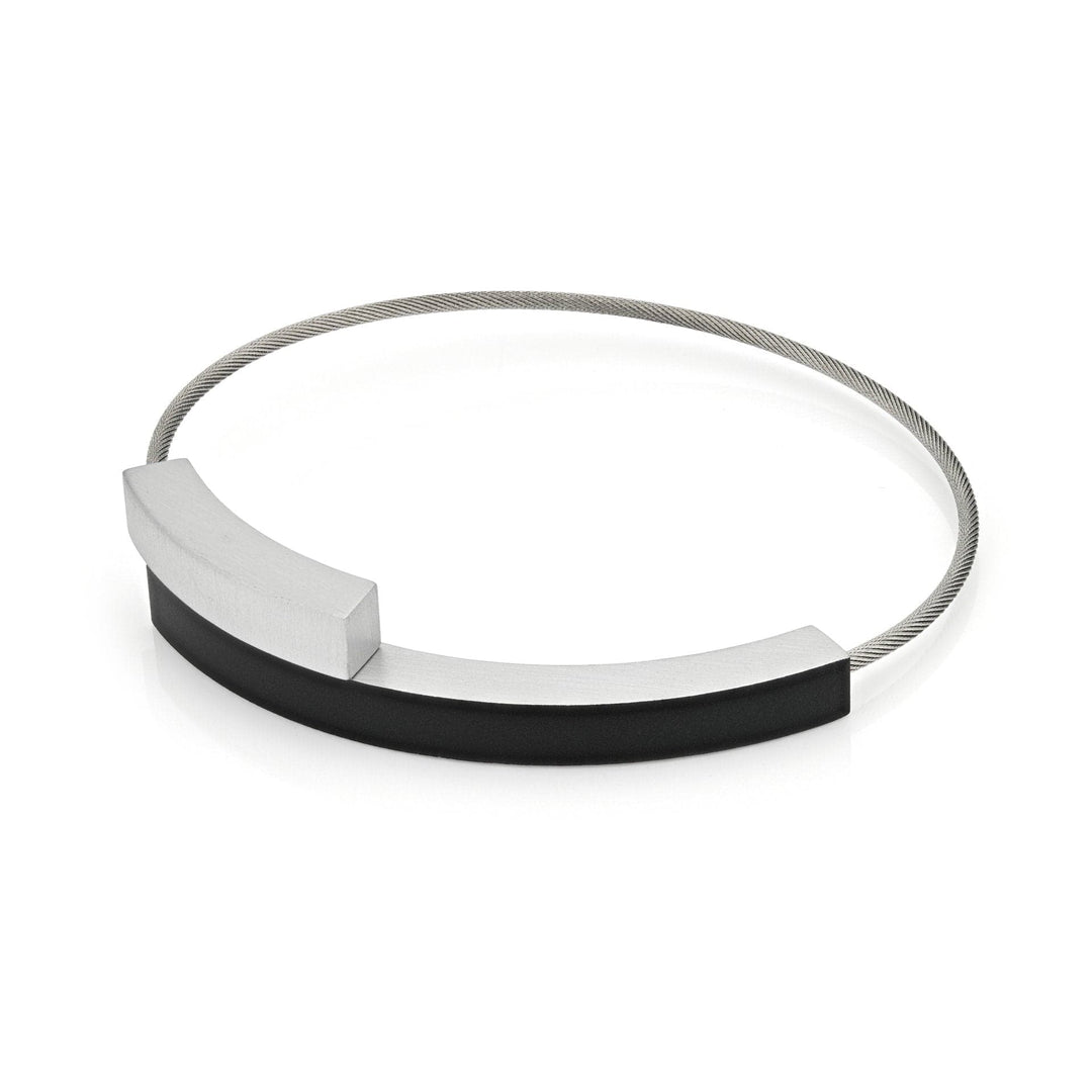 De Armband Twee boogjes Zwart A34Z van CLIC Creations is een moderne, handgemaakte zilveren chokerketting met een flexibele draadband met een strakke zwarte en zilveren rechthoekige staaf. Het minimalistische ontwerp toont contrasterende materialen en strakke lijnen, afgewerkt met een discrete magnetische sluiting voor eenvoudig dragen.