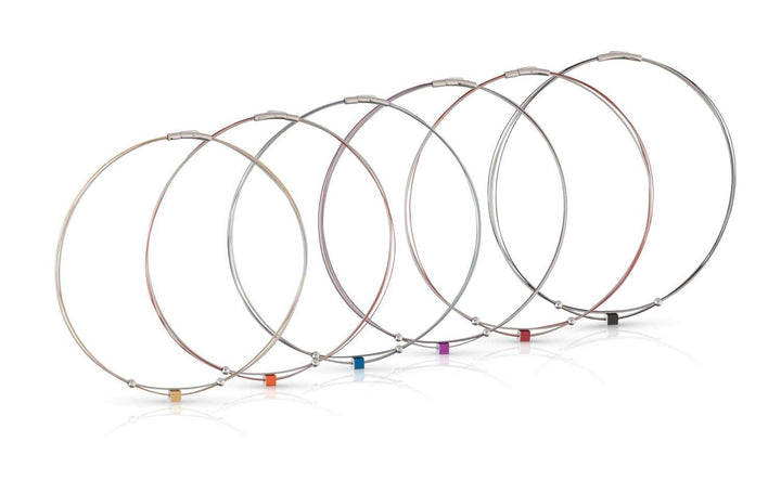 Zeven metalen draad sleutelhangers van CLIC Creations, gemaakt van chirurgisch staal, tonen sluitingen in geel, oranje, rood, paars, blauw, groen en zwart. Getoond op een witte achtergrond met kleine gekleurde kubussen voor charme; één toont het Collier Klein Kubusje Rood C230R ontwerp.