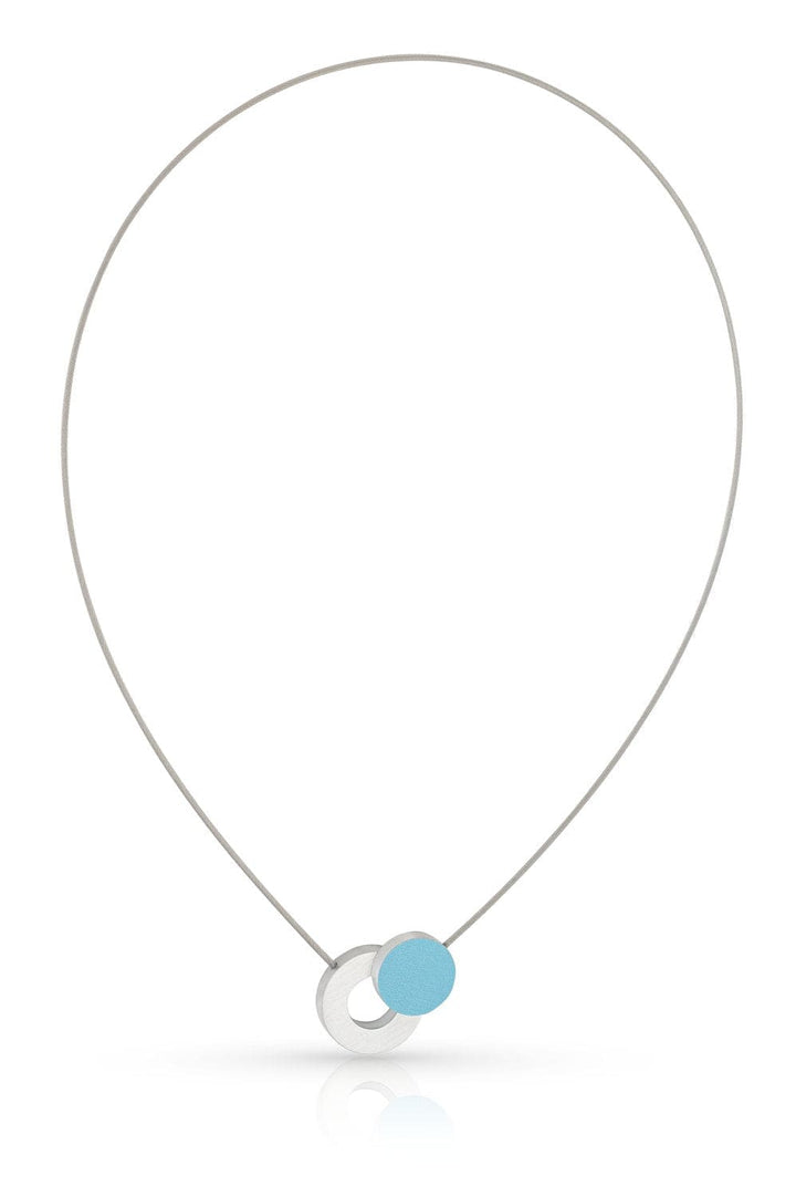 De CLIC Creations Collier Gekleurd rondje en een ring C265B heeft een minimalistisch ontwerp met een dunne zilveren ketting en in elkaar grijpende cirkels - één zilver, één lichtblauw. Handgemaakt in Nederland, het heeft een moderne stijl met een magnetische sluiting voor eenvoudig dragen.