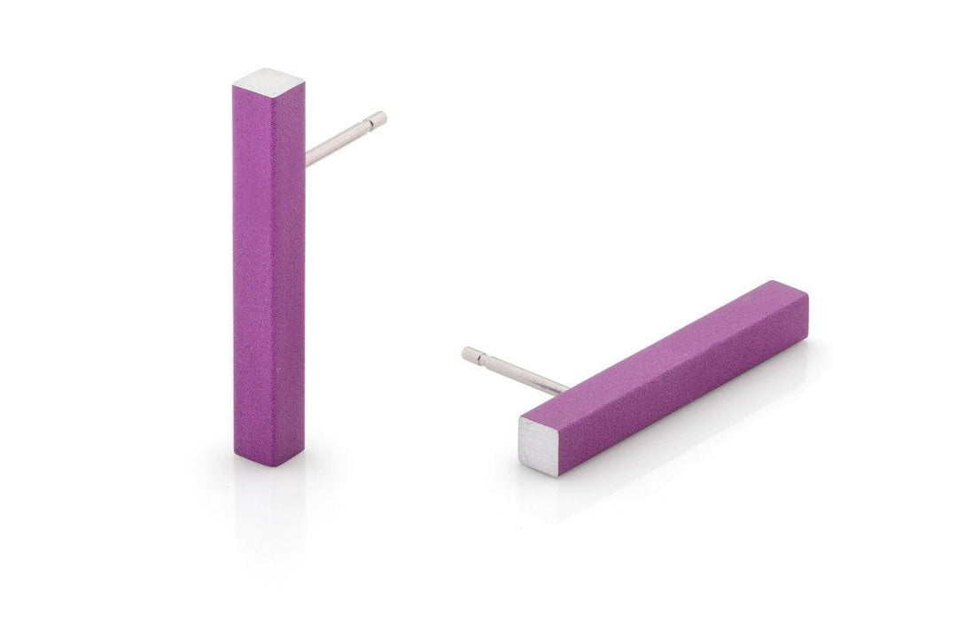 De Oorsteker Staafje Paars O26P van CLIC Creations bestaat uit twee paarse rechthoekige oorbellen van hypoallergeen aluminium met een gladde matte afwerking en zilverkleurige staafjes. Eén oorbel staat rechtop, terwijl de andere plat ligt, wat een uniek ontwerp laat zien dat met de hand is gemaakt in Nederland.