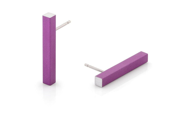 De Oorsteker Staafje Paars O26P van CLIC Creations bestaat uit twee paarse rechthoekige oorbellen van hypoallergeen aluminium met een gladde matte afwerking en zilverkleurige staafjes. Eén oorbel staat rechtop, terwijl de andere plat ligt, wat een uniek ontwerp laat zien dat met de hand is gemaakt in Nederland.