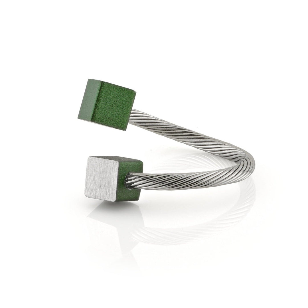 De Ring Kubusjes Groen R4GR van CLIC Creations is een gedraaide zilveren kabelarmband met open uiteinden, versierd met een matte groene kubus en een glanzende zilveren kubus. Het rust op een reflecterend wit oppervlak, wat het unieke ontwerp benadrukt.