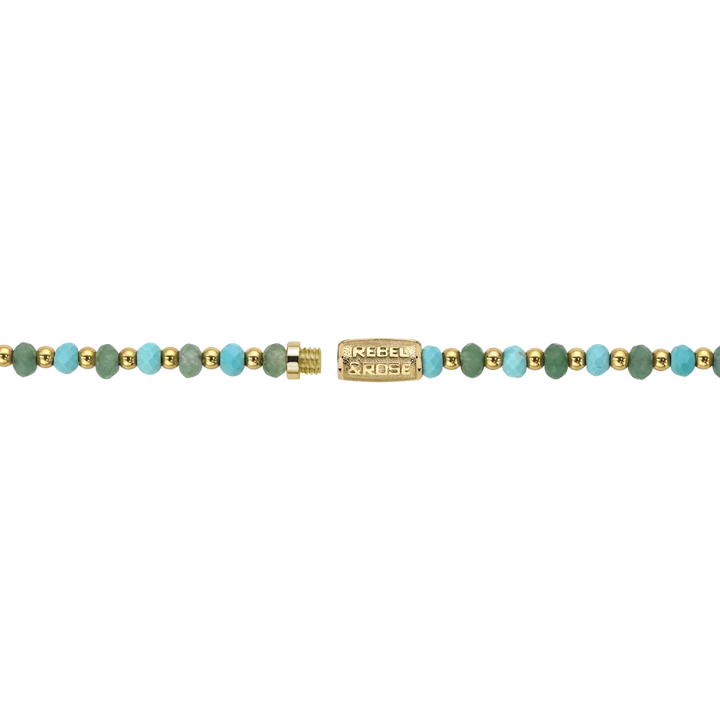 De ketting Blue Green Adventure - 4mm van Rebel & Rose heeft gouden en turquoise kralen met een 18kt vergulde rechthoekige sluiting met de gravure "Rebel Noise," op een zwarte achtergrond.