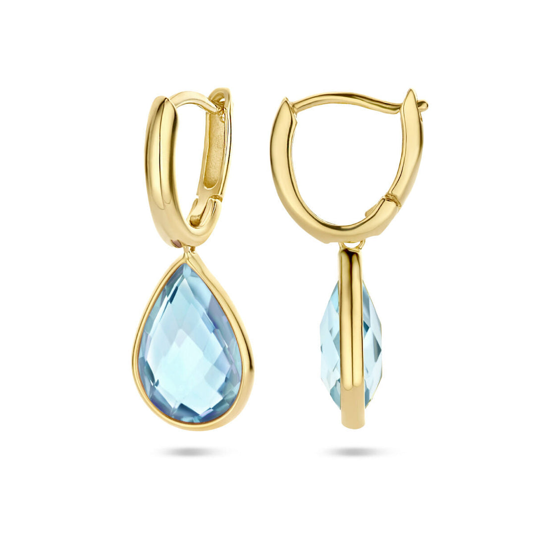 Een paar Van der Kooij Collectie klapoorringen blauw topaas 14K geelgoud met druppelvormige, facetgeslepen blauwe topaas stenen hangend aan elke ring, getoond van de voor- en zijkant op een witte achtergrond.