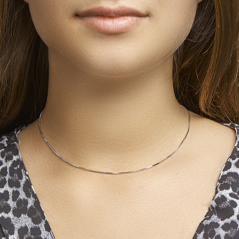 Een close-up van een vrouw met een lichte huid en steil bruin haar die de Van der Kooij Collectie collier venetiaans 1,1 mm draagt. Ze is gekleed in een grijs met zwarte dierenprint top.
