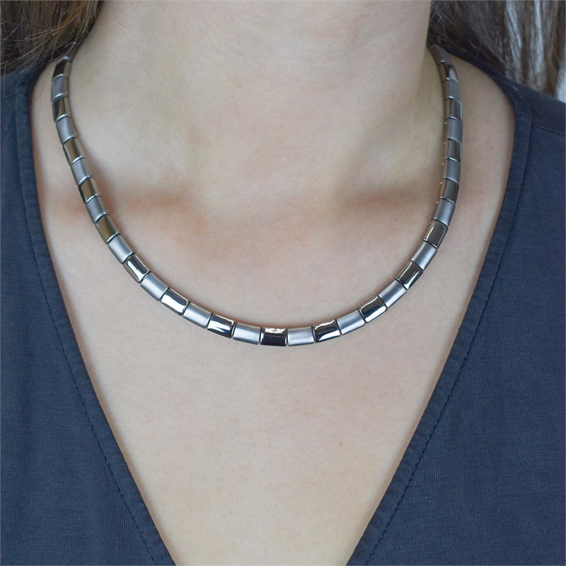 Een close-up toont een persoon die de Boccia Titanium Collier 0812-01 draagt, met mat zilveren rechthoekige schakels, in combinatie met een donker V-hals shirt. Het Boccia collier zit soepel om de hals.