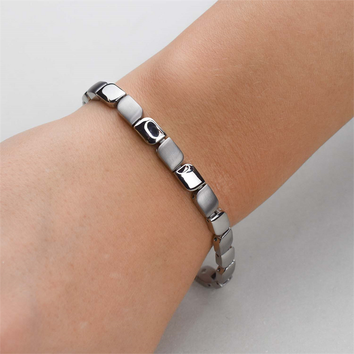 Een close-up van de pols van een persoon die de Boccia Titanium Armband 03007-01 draagt, met een zilverkleurig, modern rechthoekig schakelontwerp, tegen een effen lichtgekleurde achtergrond.