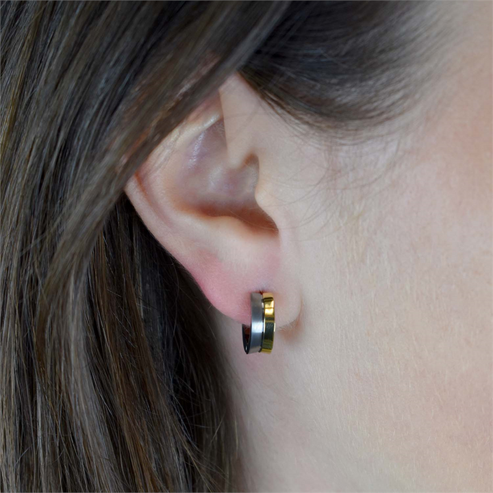 Close-up van een persoon met een lichte huidskleur en steil bruin haar die Boccia Titanium Oorringen Bicolor 0511-01-kleine, ronde oorbellen in zwart en goud van Boccia draagt.