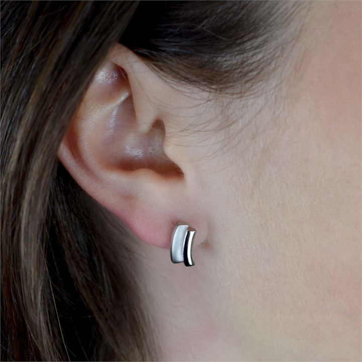Close-up van het oor van een persoon met Boccia Titanium Oorstekers 0561-01, met een modern, gebogen zilveren design. Deze minimalistische titanium oorstekers van Boccia zijn tweekleurig en mat, afgebeeld tegen een neutrale achtergrond die hun elegantie benadrukt.