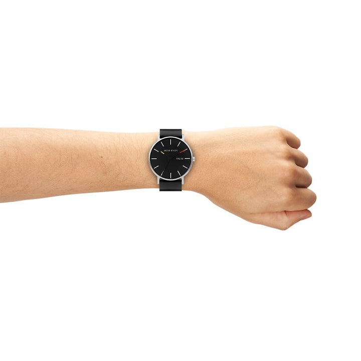 De arm van een persoon met een minimalistisch Jacob Jensen quartz polshorloge, model 162, met een zwarte band en ronde zwarte wijzerplaat met witte uurmarkeringen en wijzers. Het titanium ontwerp van het horloge is eenvoudig en elegant tegen een effen witte achtergrond.
