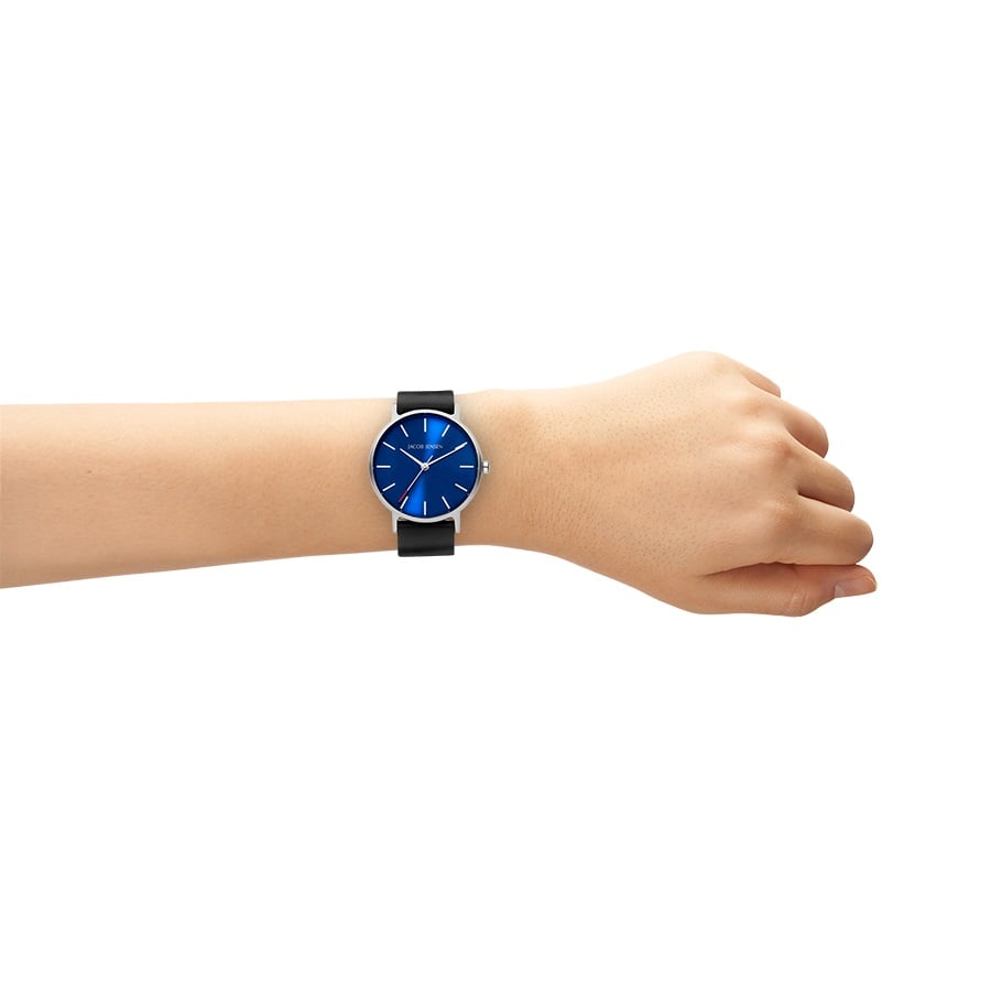 Om de pols draagt het Jacob Jensen 171 horloge tegen een witte achtergrond, met een saffierblauwe wijzerplaat, zwarte band en minimalistisch design met dunne zilveren markeringen en wijzers, elegant omhuld door titanium.