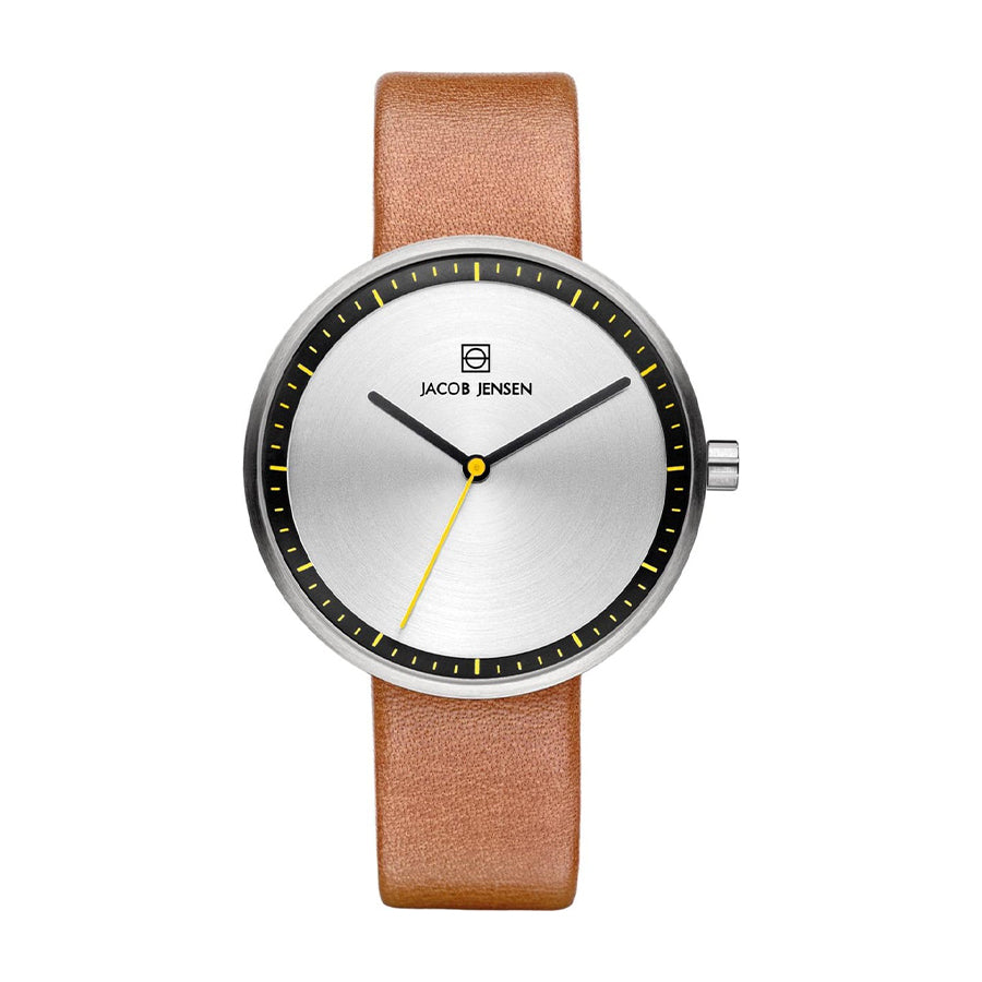 De Jacob Jensen 281 is een strak quartz polshorloge met een ronde zilveren wijzerplaat, minimalistisch design, zwarte uurmarkeringen, gele secondewijzer en bruine leren band. Mineraal glas beschermt de merknaam, elegant weergegeven onder de 12-uurspositie.