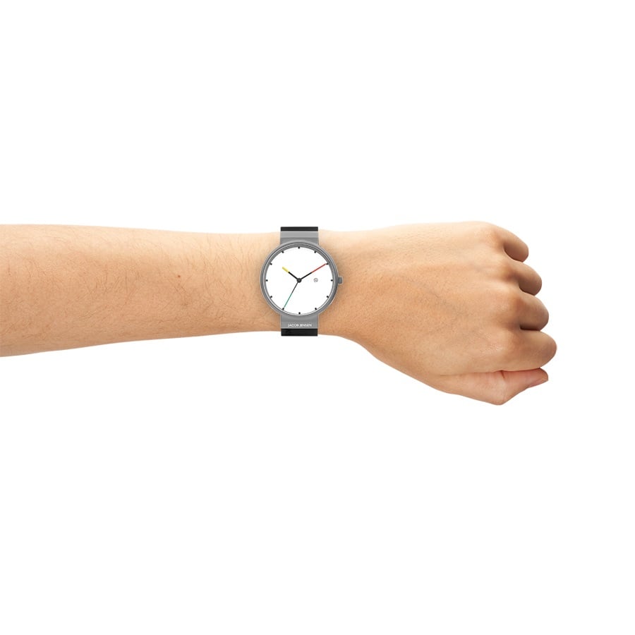 Een linkerhand toont elegant de Jacob Jensen 642, een minimalistisch analoog horloge met een strak titanium design, zwarte band en witte wijzerplaat. Het quartz-aangedreven horloge toont de tijd rond 10:10 tegen een effen witte achtergrond.