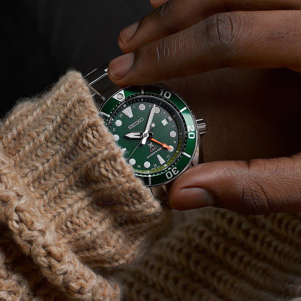Met een gebreide beige trui aan, past iemand zijn Seiko Prospex heren horloge SFK003J1 aan. Dit horloge heeft een solar uurwerk met een groene wijzerplaat, witte uurmarkeringen en een draaibare lunette met minutenmarkeringen.