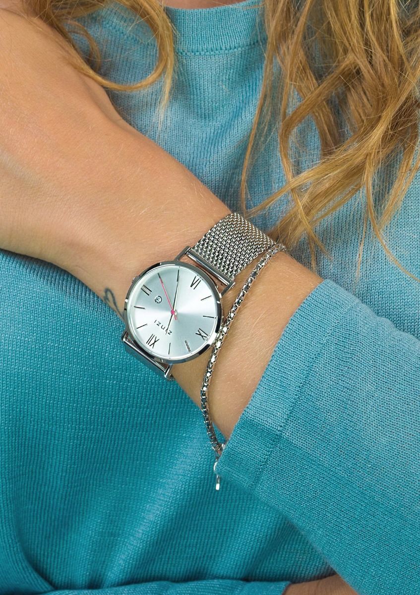 Iemand draagt het Zinzi Zilverkleurig Horloge Staal Ziw502 M met een witte wijzerplaat en Romeinse cijfers, gecombineerd met een delicaat zilveren schakelarmbandje, rust zijn arm op een groenblauw topje. Lichtbruin haar is gedeeltelijk zichtbaar.